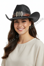 A woman wearing a black textured cowboy hat with a brown band and silver concho detail, paired with a cream-colored top, set against a plain white background with a diagonal watermark.