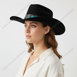 A woman in profile wearing a black wide-brim fedora hat with a patterned band and a cream-colored collared shirt, photographed against a light gray studio background.