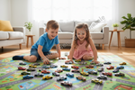 Two children sitting on a colorful play mat with many toy cars in a bright living room. The boy wears a blue shirt and denim shorts, and the girl wears a pink dress.